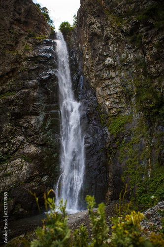 A high waterfall with white splashes of water descends from the mountain and sparkles in the sun. Attraction of Georgia Gveleti waterfall © Ольга Симонова