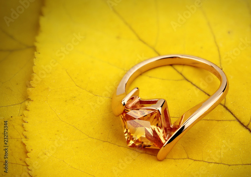 Jewelry ring with gemstone on yellow leaves background, copy space photo