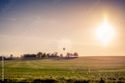 A hot air balloon flying over the field at sunset.