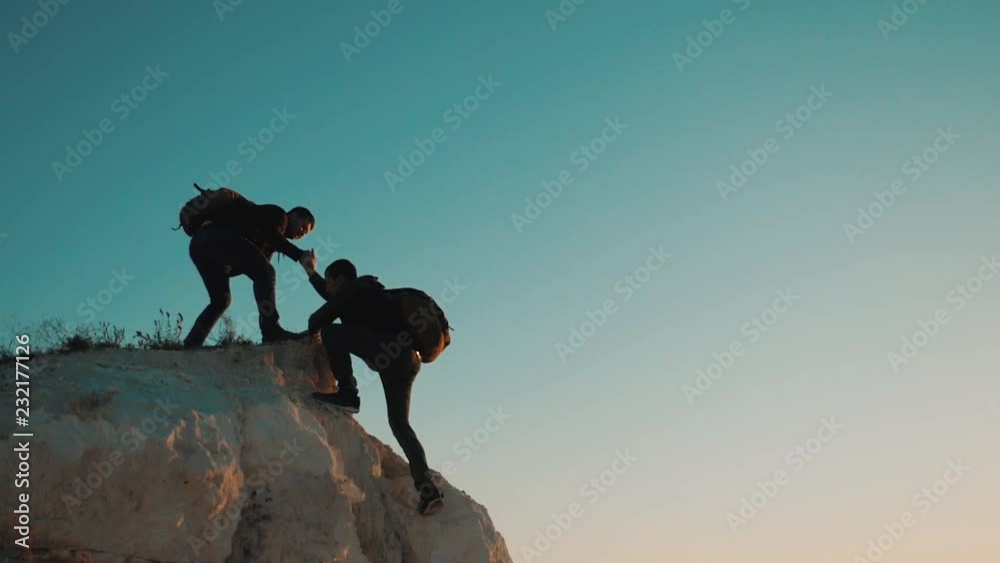 Teamwork friendship hiking help each other trust assistance silhouette in mountains. Backpacker helps to his friend to climb to rock. two travelers help stretching hand tourist lifestyle concept