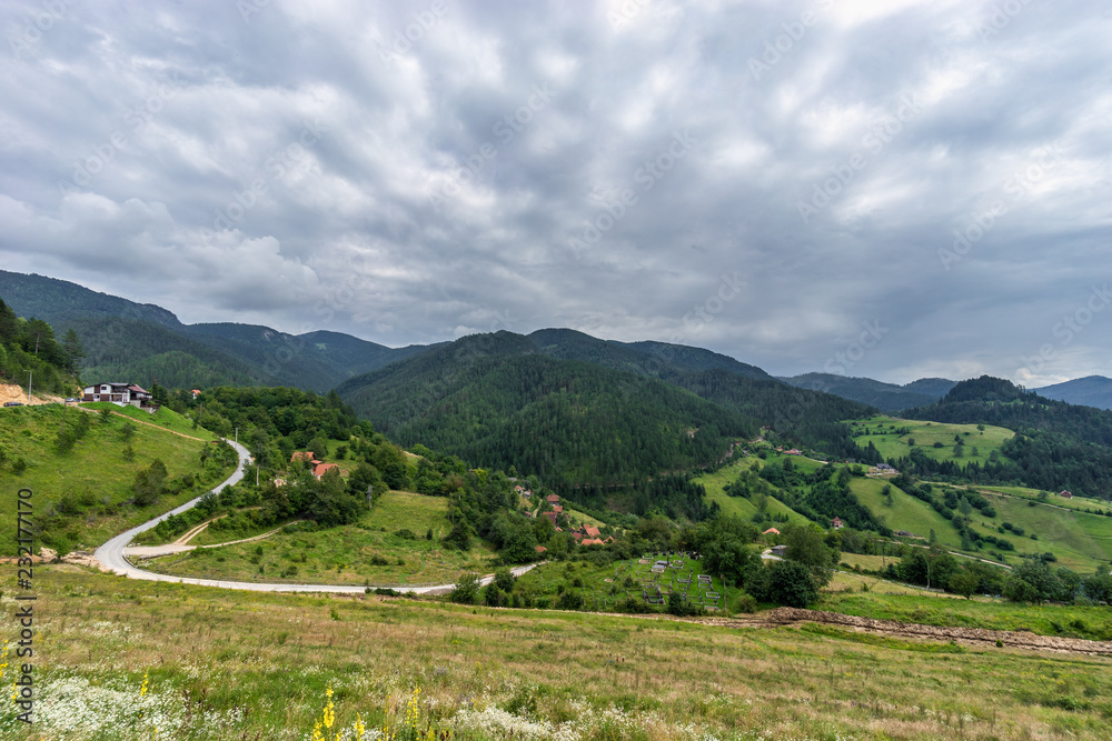 View on Lazici village and green hills overgrown with spruce and pine in Serbia in cloudy summer day