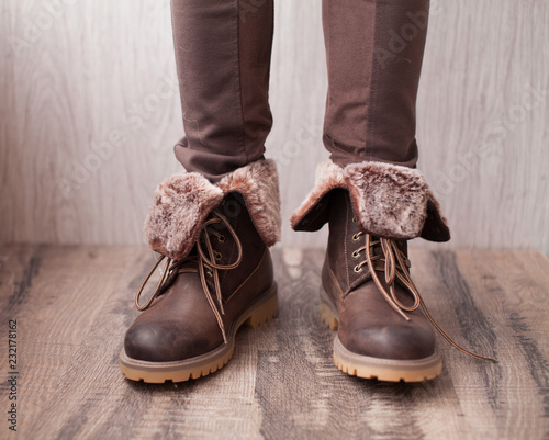 Female legs wearing warm winter boots standing on a wooden floor