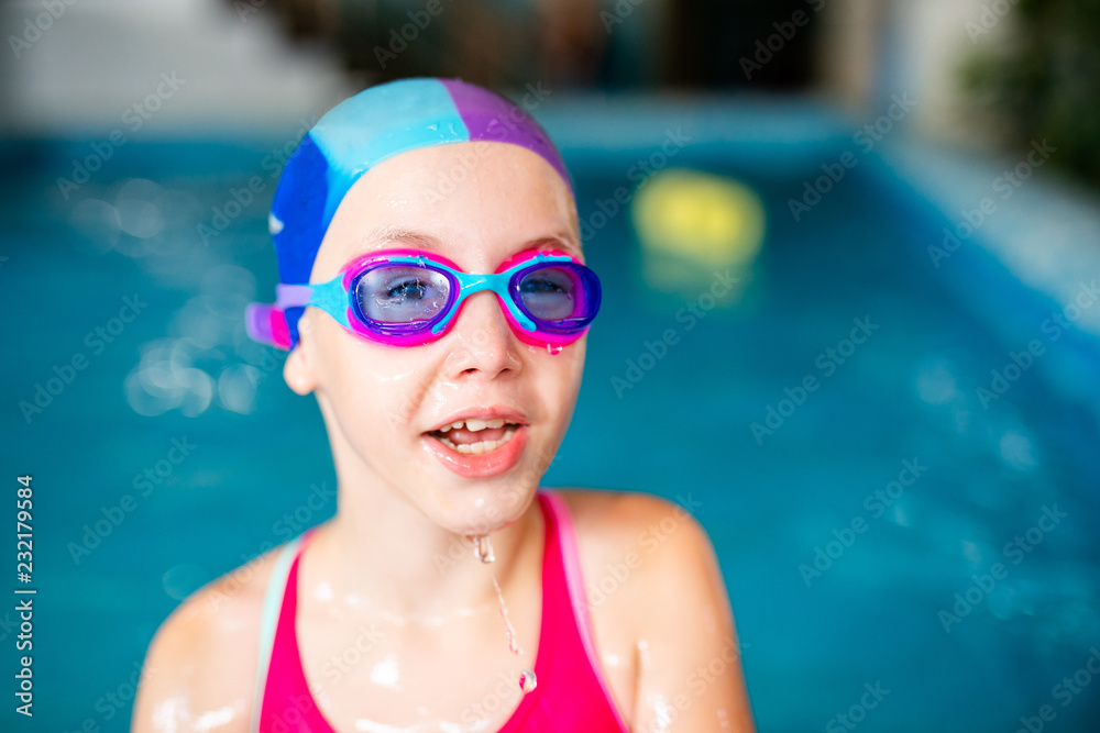 Happy girl with swimming hat and glasses in the blue pool indoor