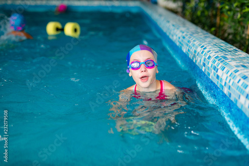 Happy girl with swimming hat and glasses in the blue pool indoor photo