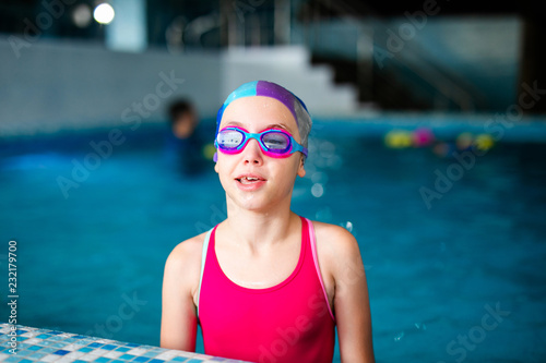 Happy girl with swimming hat and glasses in the blue pool indoor photo