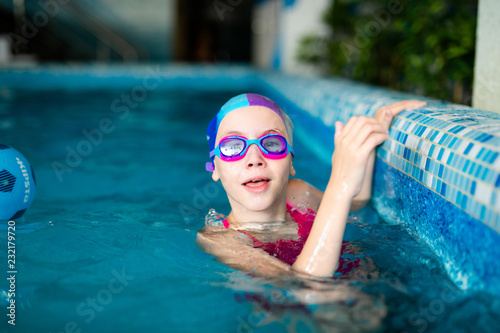 Happy girl with swimming hat and glasses in the blue pool indoor