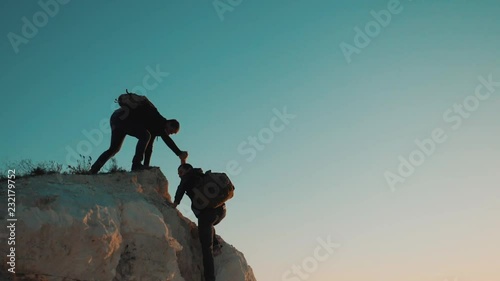 Teamwork friendship hiking help each other trust assistance silhouette in mountains. Backpacker helps to his friend to climb to rock. two travelers help stretching hand lifestyle tourist concept photo