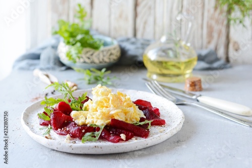 Scramble of eggs with carpaccio of baked beets with walnuts, aromatic herbs and arugula on a plate. Delicious healthy breakfast. Beet carpaccio with sauce on a white plate.