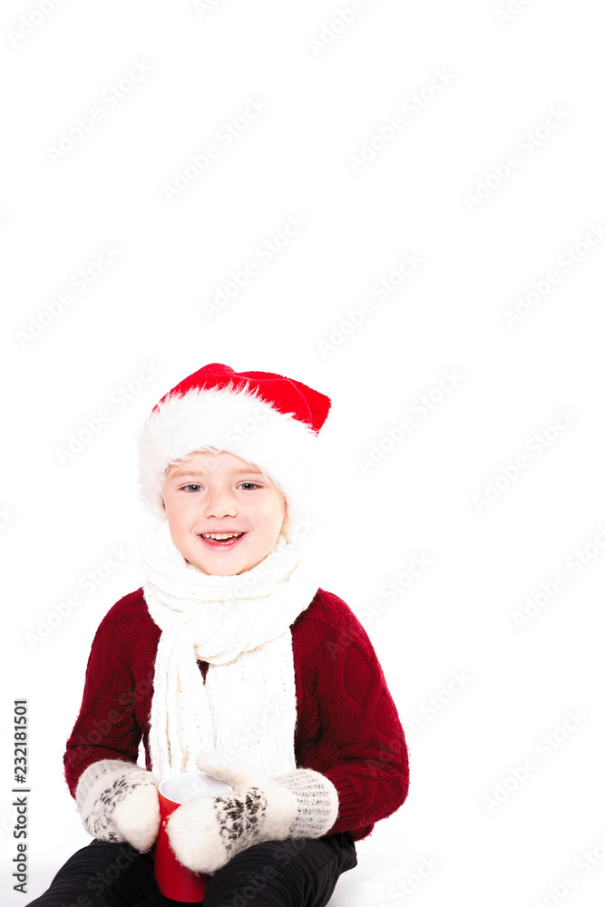 Merry Christmas and happy New year! Cute happy little boy holding red cup. Kid enjoy holiday santa hat. Portrait kid on light background isolated. Happy Child with place for text Merry Christmas and happy New year! Cute happy little boy holding red cup. Kid enjoy holiday santa hat. Portrait kid on light background isolated. Happy Child with place for text