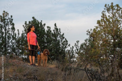 A hispanic woman is hiking with a dog, at sunset, in the Rocky Mountains near Denver, Colorado, USA