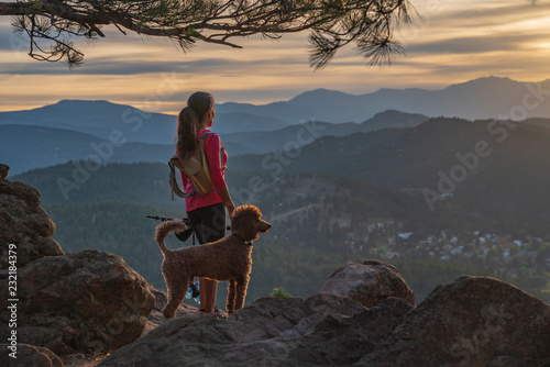 A hispanic woman is hiking with a dog, at sunset, in the Rocky Mountains near Denver, Colorado, USA