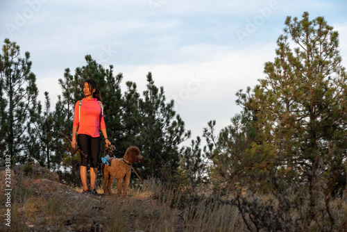 A hispanic woman is hiking with a dog, at sunset, in the Rocky Mountains near Denver, Colorado, USA