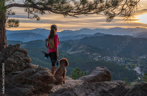 A hispanic woman is hiking with a dog, at sunset, in the Rocky Mountains near Denver, Colorado, USA