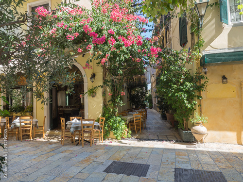 Corfu old town cobble stone street with restaurant and cafe tables and flower garlands, summer sunny day, Kerkyra townCorfu island, Ionian islands, Greece