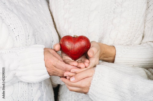 three womans holding red heart in hands.  Love concept to Valentine's Day . Women of different ages in warm sweaters hold a wooden heart