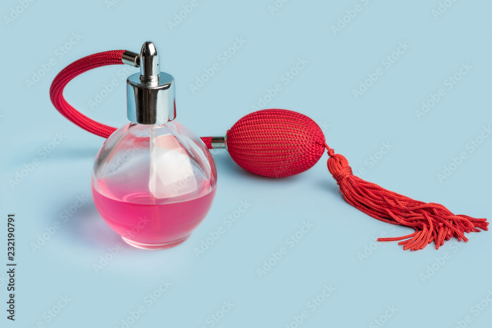 Bright pink perfume in a glass transparent bottle with red vintage style sprayer with an airbag and tassel on pastel baby pink background shot with studio light