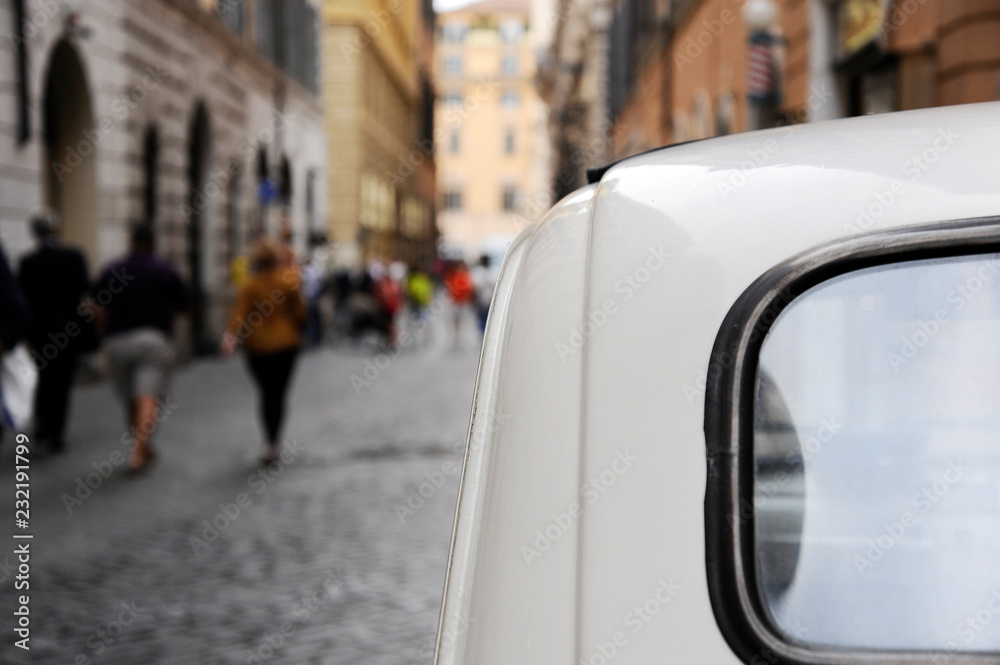 A parked Fiat 500 in the streets of Rome, some people on the background ...