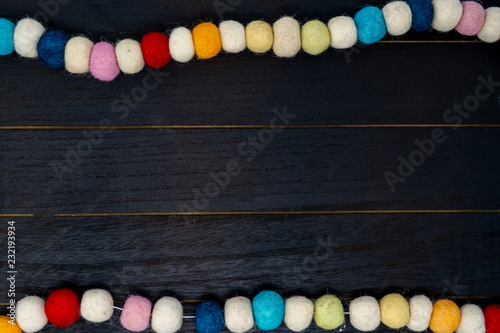 Pretty colorful rainbow pom pom fabric garland over black wood background. Useful for birthday projects or non traditional Chistmas backgrounds