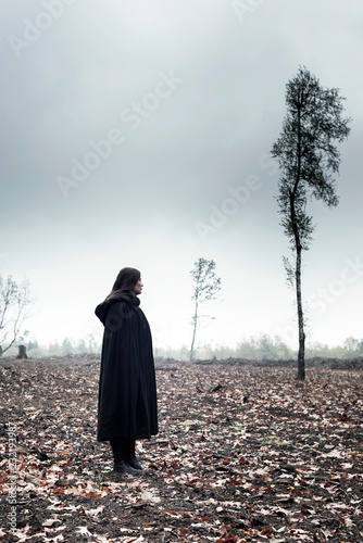 Woman in black cape in moody countryside.
