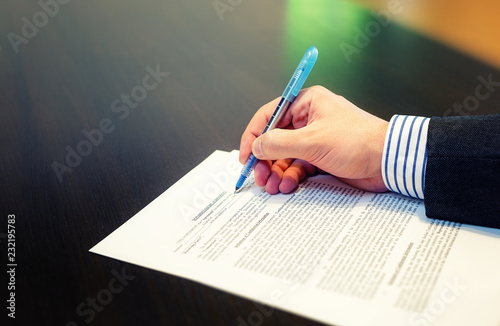 Cropped closeup of a man hand filling in Non Disclosure Agreement (NDA). Reading and signing business concept