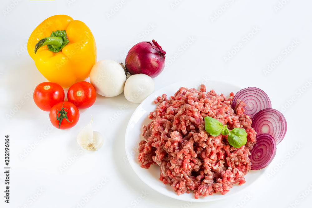 fresh raw minced beef in a white plate close up with pepper, onion and tomatoes, raw ingredients for stuffed peppers