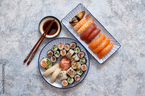 Asian food assortment. Various sushi rolls placed on ceramic oriental style plates. Soy souce and chopsticks on sides. Grungy dark background with copy space.