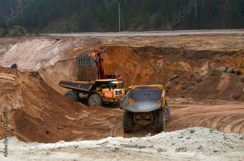 Large quarry dump truck. View of the large sand pit. Production useful minerals. Mining. Excavator loading sand into dumper truck.