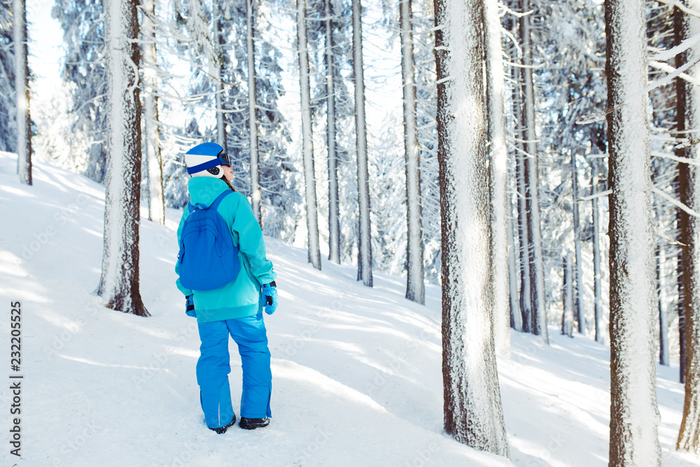 Naklejka premium A beautiful girl in winter clothes, a blue helmet and a green jacket is having a great time in the mountains. Concept of travel, leisure, freedom, sport. Beautiful nature, places, great weather.