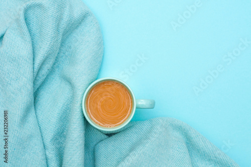 A cup of coffee with milk, a warm bedspread on a bright blue background. Top view