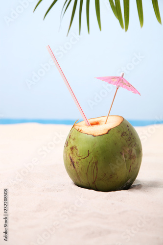 Coconut with straw and drink umbrella on white sand