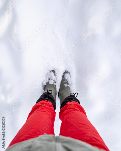 Human legs in warm boots stand on a snowy footpath, on a winter frosty day.