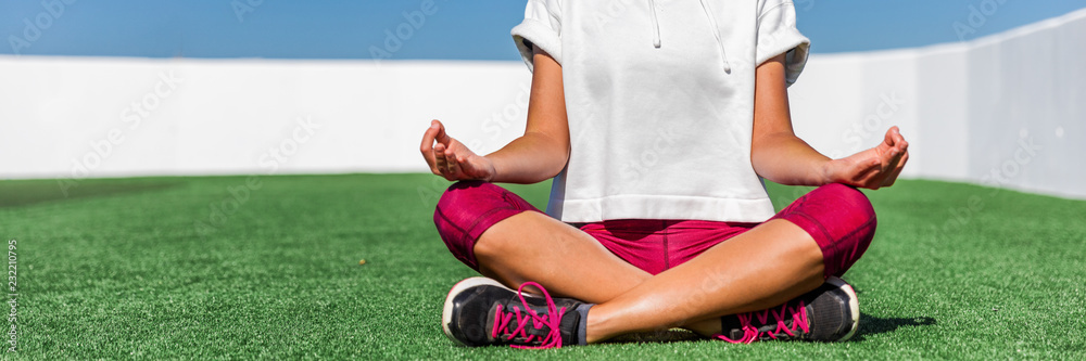 Yoga fitness sport woman meditating in lotus pose sitting on grass. Panorama banner crop of activewear leggings and shoes. Lower body legs and feet.