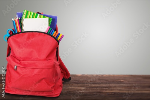 Open red school backpack on wooden table and wall background.