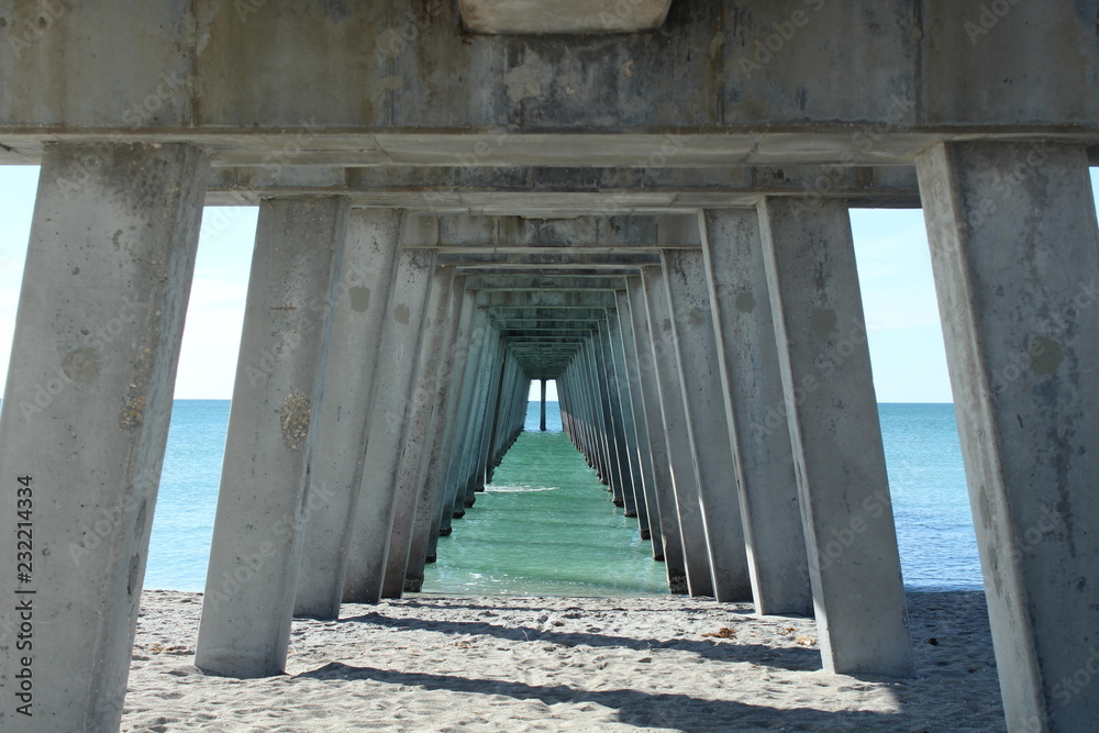 underneath a fishing pier on the gulf coast of Florida with pretty blue green water on the beach