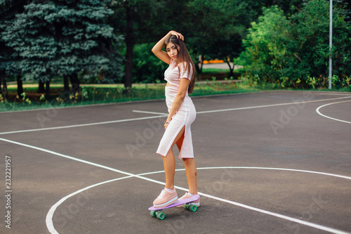 Portrait of a smiling charming brunette female standing on her skateboard on a basketball court. © Smile
