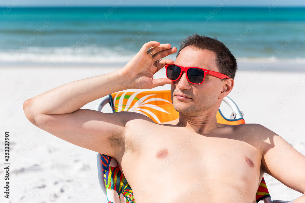 Man muscular face closeup lying on beach lounge chair during sunny day with red sunglasses in Florida with ocean water Man muscular face closeup lying on beach lounge chair during sunny day with red sunglasses in Florida with ocean water