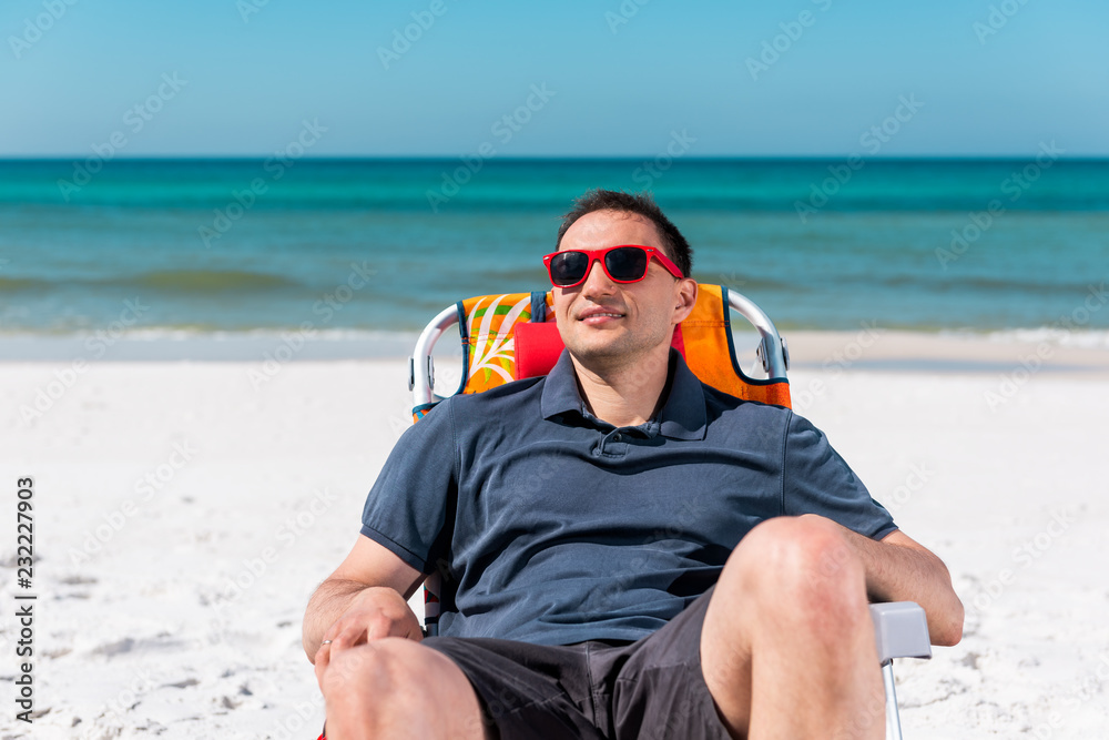 Happy man smiling face closeup lying on beach lounge chair during sunny day with red sunglasses in Florida panhandle with ocean water