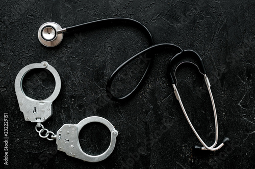 Medical lawsuit. Arrest for medical crime concept. Handcuff near stethoscope on black background top view
