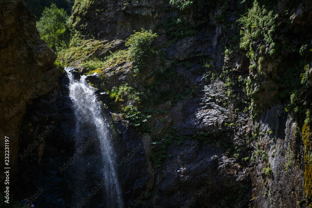 A high waterfall with white splashes of water descends from the mountain and sparkles in the sun. Attraction of Georgia Gveleti waterfall A high waterfall with white splashes of water descends from the mountain and sparkles in the sun. Attraction of Georgia Gveleti waterfall