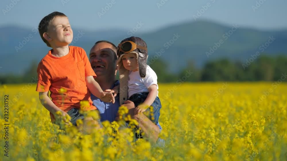 Father with two sons appearing from blossom rape field, have fun in nature Father with two sons appearing from blossom rape field, have fun in nature