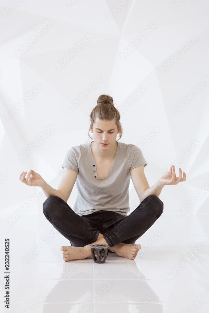 Fototapeta premium Full length of a young man meditating in lotus position against white polygon background