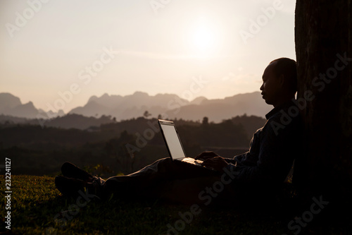 Businessman sitting on grass is working on laptop in the park.