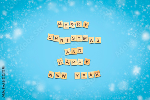 Text of Happy Christmas and Happy New Year laid out of wooden plates with letters on a blue background. Minimalism. Flat lay, top view