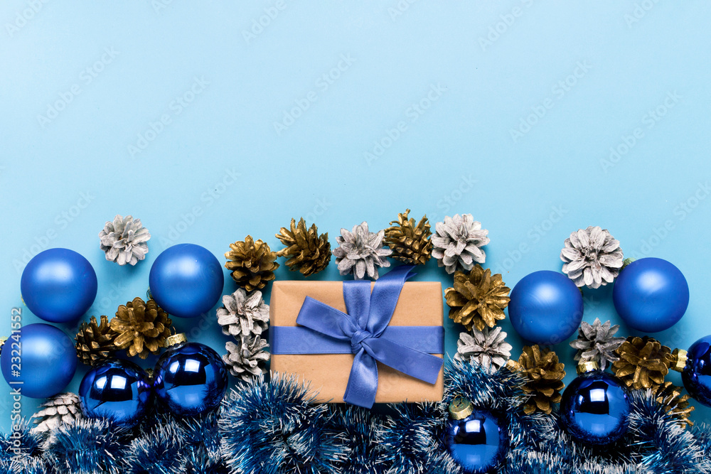 Gift box with blue ribbon, Christmas-tree decorations, balls and white and gold pine cones on a blue background. Concept of Merry Christmas and Happy New Year. Minimalism. Flat lay, top view