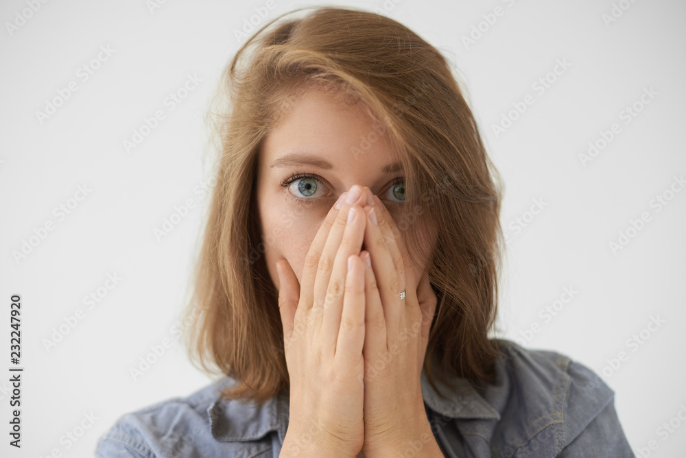 Close up picture of frightened young woman with loose hairdo covering face with both hands and staring at camera with scared look, being stressed or terrified with something. Human emotions Close up picture of frightened young woman with loose hairdo covering face with both hands and staring at camera with scared look, being stressed or terrified with something. Human emotions
