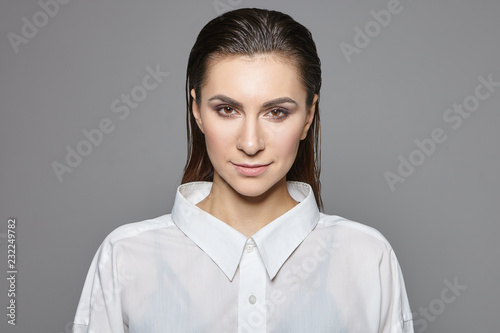 Femininity, masculinity and androgyny concept. Isolated shot of successful beautiful young brunette businesswoman in stylish formal white shirt looking at camera with confident expression, smiling