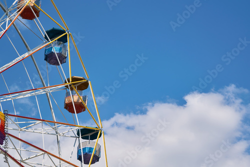 A large Ferris wheel at an amusement Park on a background of blue sky. Several cabins with roofs in the form of umbrellas. The sturdy construction is decorated with colorful bulbs.