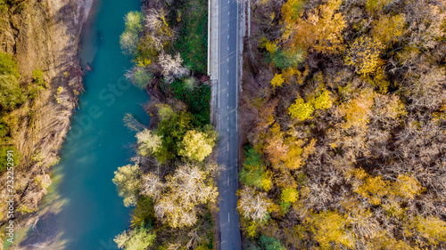 Beautiful landscape with a rural road along a mountain river, autumn trees with green, yellow, red leaves. Top view. Aerial view from a drone