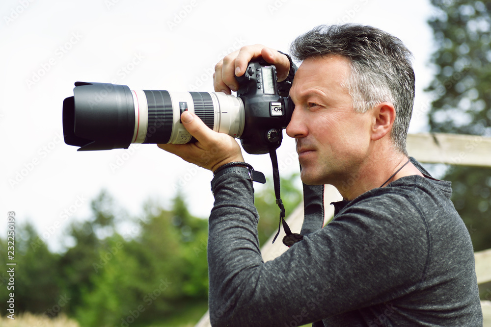 Man professional photographer with digital camera takes photos outdoor. Photo camera in male hands. Destination photographer at work. Paparazzi with telephoto lens