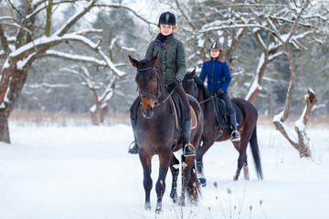 Two young women riding horses in winter park